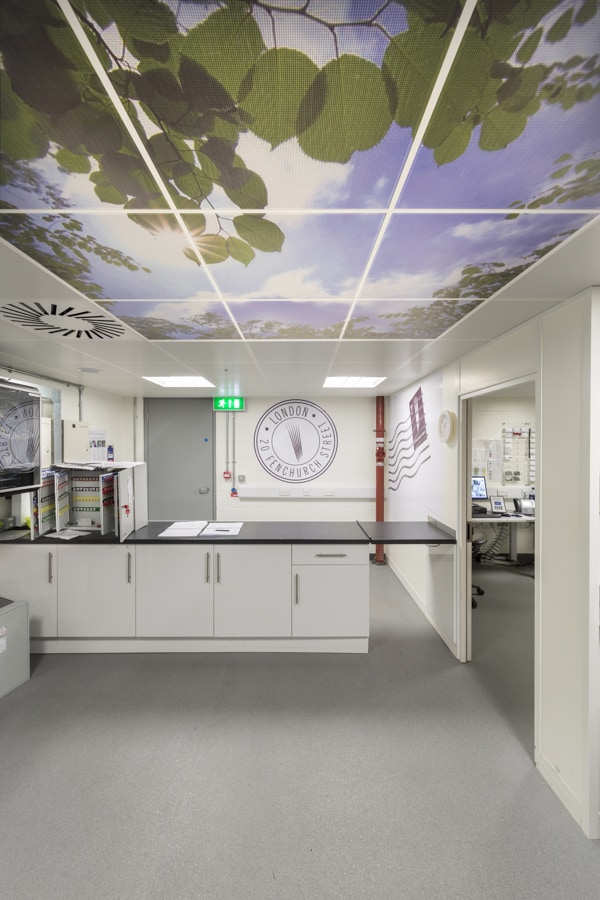 Image showing the internal view of a post room. The ceiling design features a photograph of a view of a blue sky seen through tree leaves. The back and left hand walls are decorated with large postage stamp graphics.