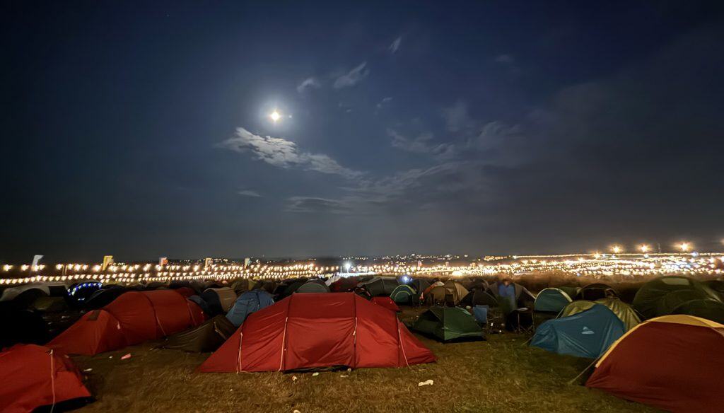 Night-time view across a festival camping site towards the main arena