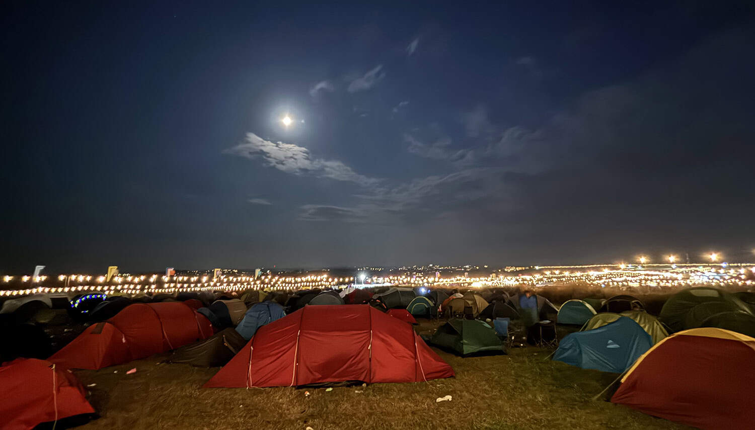 Night-time view across a festival camping site towards the main arena